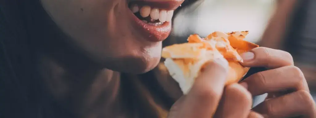 Funny brunette girl in yellow sweater eating pizza at restaurant.